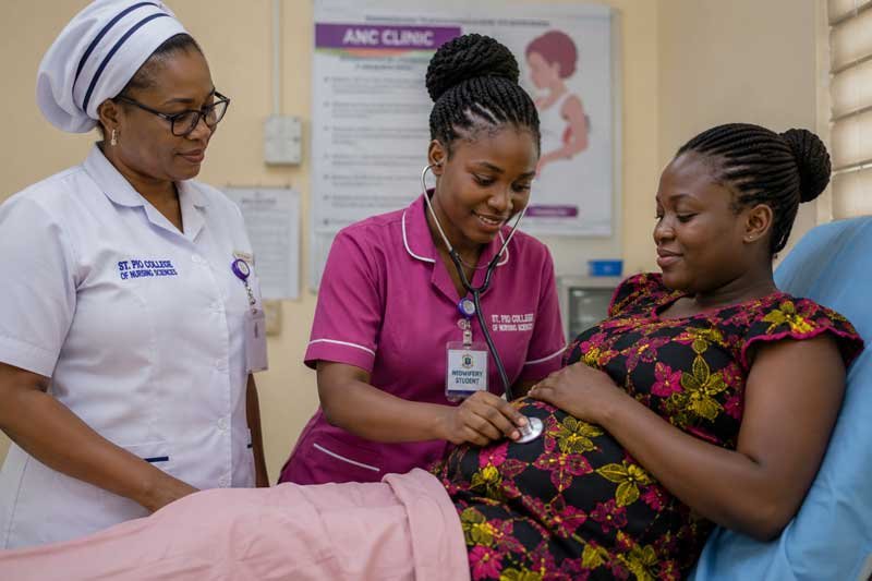 A Black Nigerian midwifery student assisting a pregnant woman during antenatal care or holding a newborn baby alongside a supervising midwife